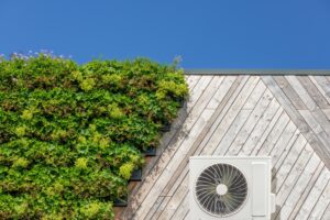 Thermopompe air-air sur un bâtiment vert et durable recouvert de plantes suspendues fleuries.