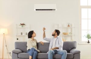 Jeune couple de famille assis ensemble sur un canapé dans le salon et allumant l'air conditionné. Paramètres de réglage avec télécommande pour une température intérieure confortable.