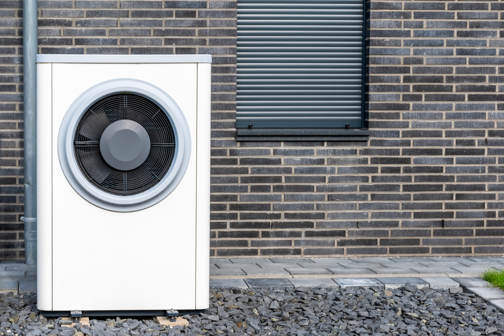Module extérieur d’un système de chauffage à thermopompe moderne situé dans le jardin de façade en pierre d’une maison résidentielle.