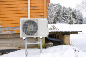 Air to water heat pump near an old wooden house in winter. air water heatpump, low emission renewable energy close up