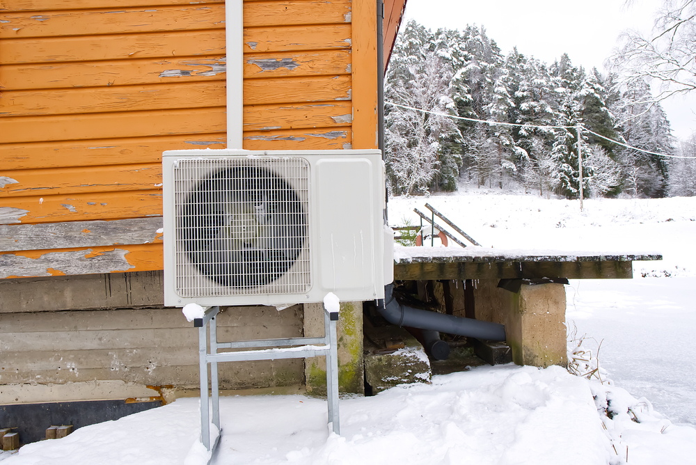 Air to water heat pump near an old wooden house in winter. air water heatpump, low emission renewable energy close up