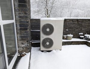 A snowy view of an outside unit for an air source heat pump.