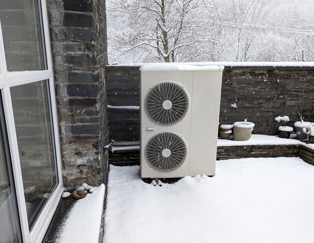 A snowy view of an outside unit for an air source heat pump.