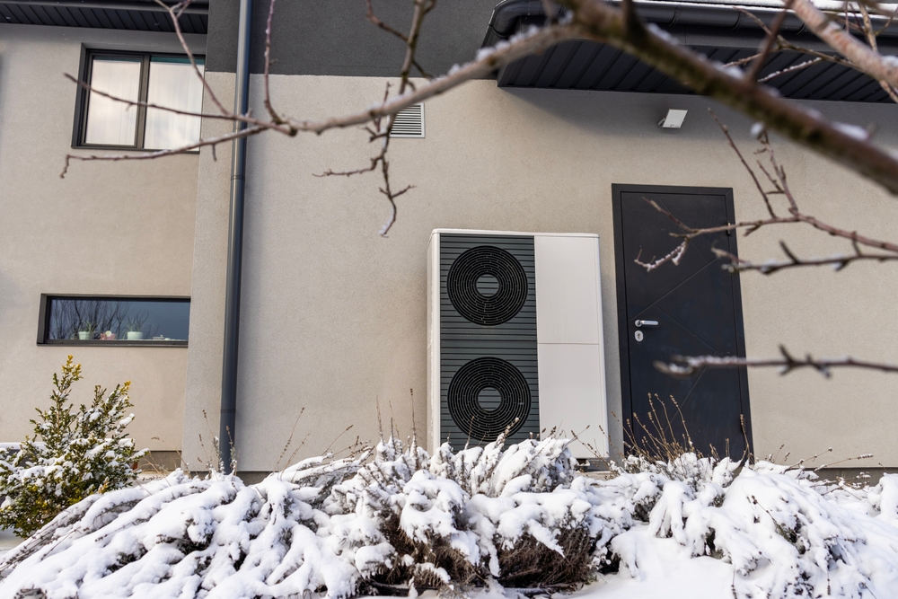 Modern heat pump unit outside a house in winter, providing energy-efficient heating in cold weather.