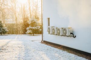 A modern air source heat pump installed on the wall of a modern residential building in winter season. The outdoor unit of an air-source heat pump in winter time.